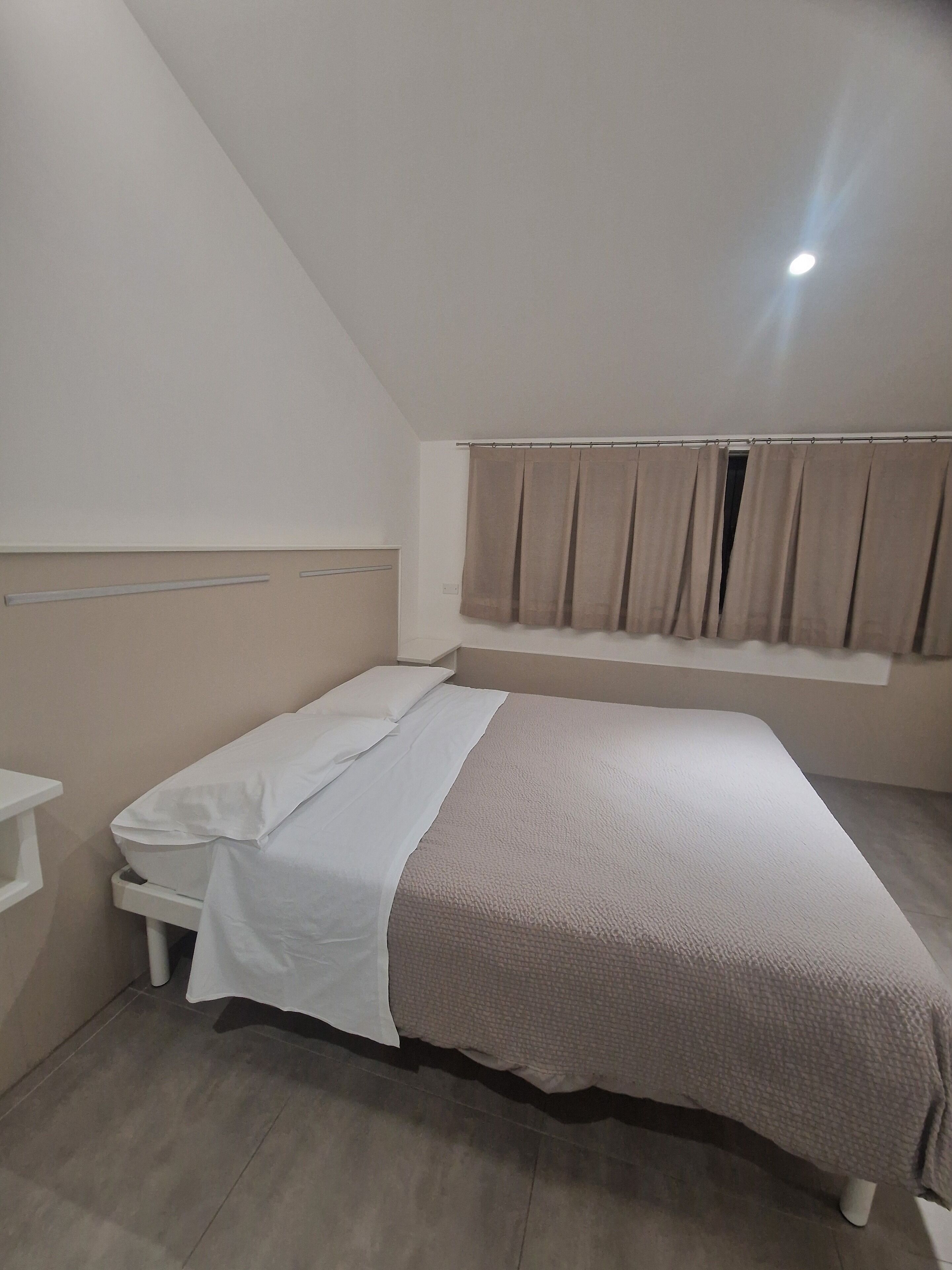 Un dormitorio con cama, ventana con cortinas, mesita de noche y cabecero.