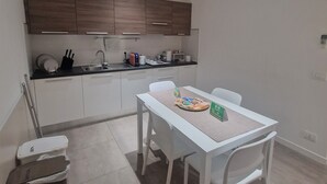 A modern kitchen with white cabinets, a dining table with chairs, and a trash bin. - Bed&Bike (Aulla)