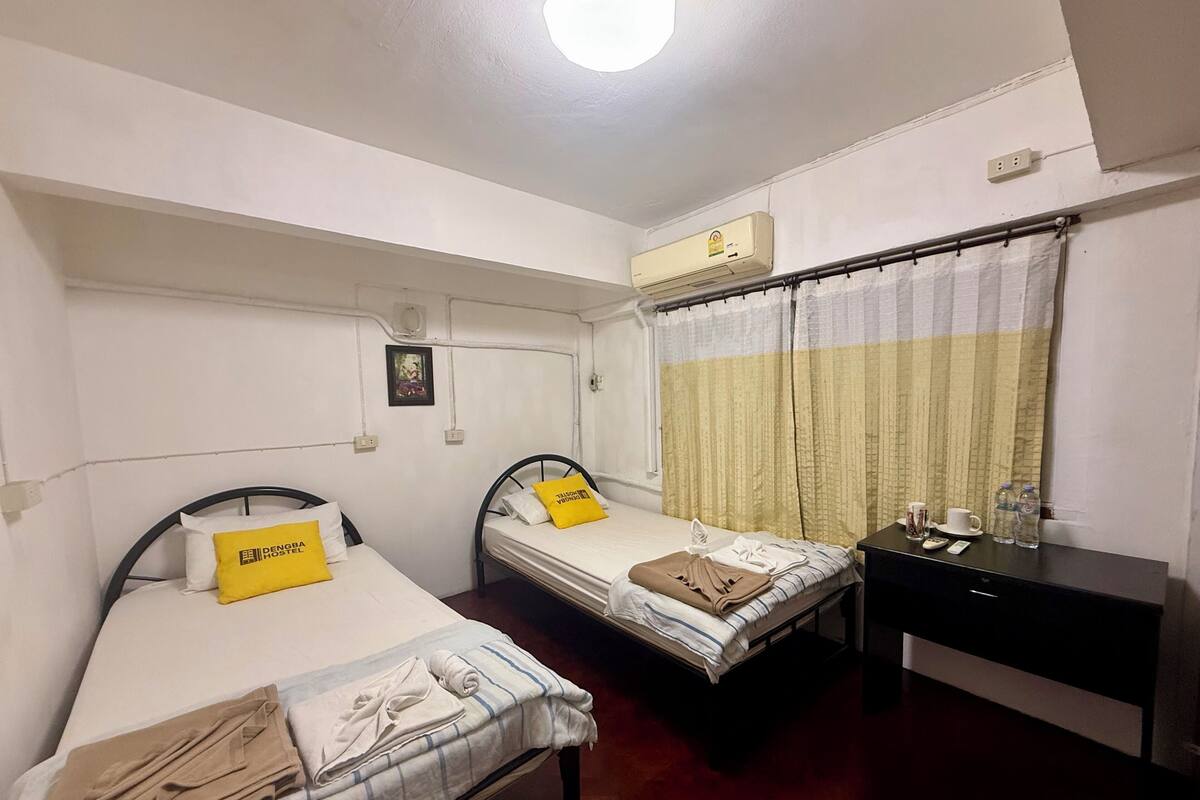 A small, clean room with two single beds, a desk, and a window with curtains.