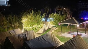 A campsite with tents and a covered seating area, surrounded by trees and illuminated by string lights. - Red Leaf Resort & Cafe (Kasol)