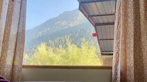A room with a view of a mountain and trees through a window with patterned curtains. - Red Leaf Resort & Cafe (Kasol)