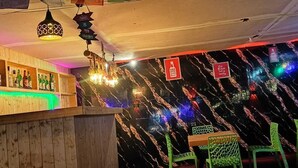 A bar area with a wooden counter, green chairs, and a black marble wall with colorful lights. - Red Leaf Resort & Cafe (Kasol)