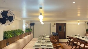 Une longue table à manger entourée de nombreuses chaises, un ventilateur de plafond et des luminaires suspendus.
