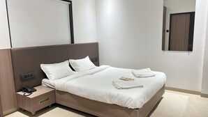 Un lit bien fait, avec du linge de lit blanc, une table de chevet avec un téléphone et un miroir fixé au mur.