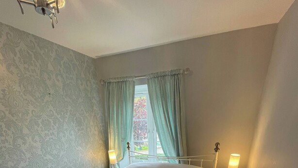 A bedroom with a bed, two bedside tables, a window with curtains, and a wall with a patterned wallpaper. - Room-chew Valley Retreat Suite (Bristol)