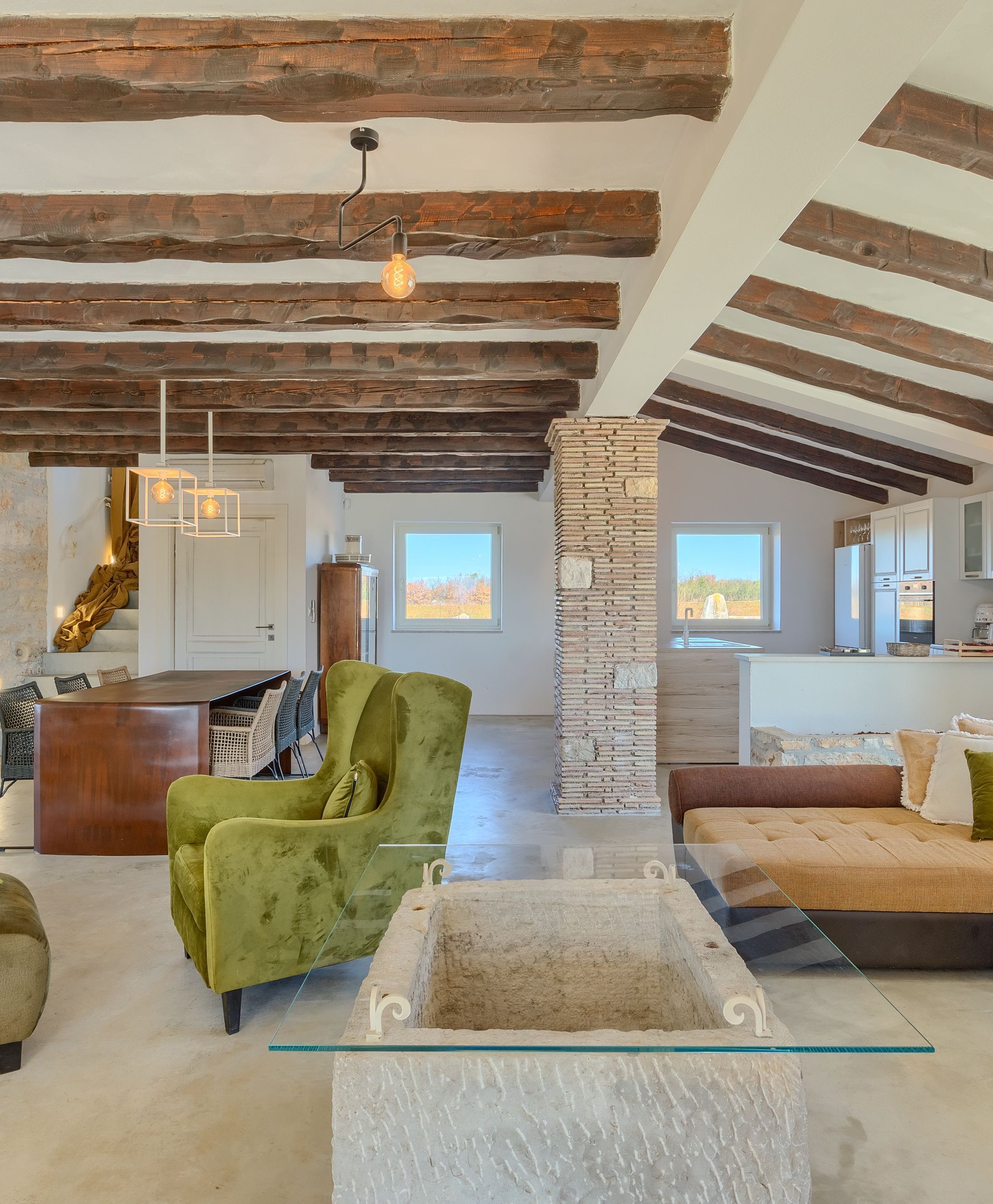 A spacious loft with exposed wooden beams, a stone fireplace, and a large window offering a view of the outdoors.