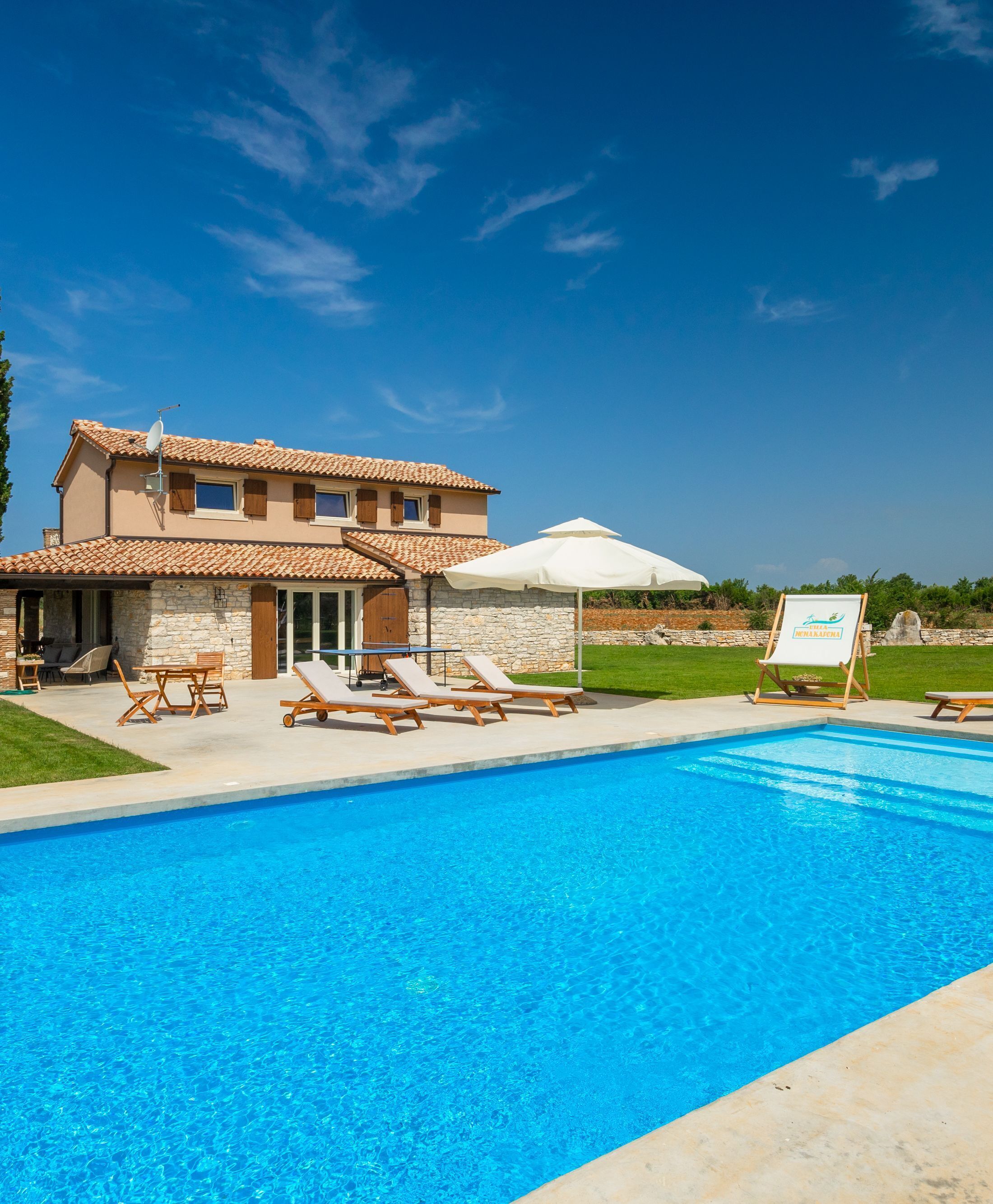 A two-story house with a swimming pool, lounge chairs, and a signboard.