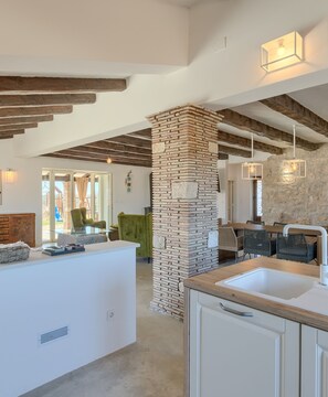 Uma cozinha moderna com ilha central, parede decorada com pedra e vigas de madeira aparente.