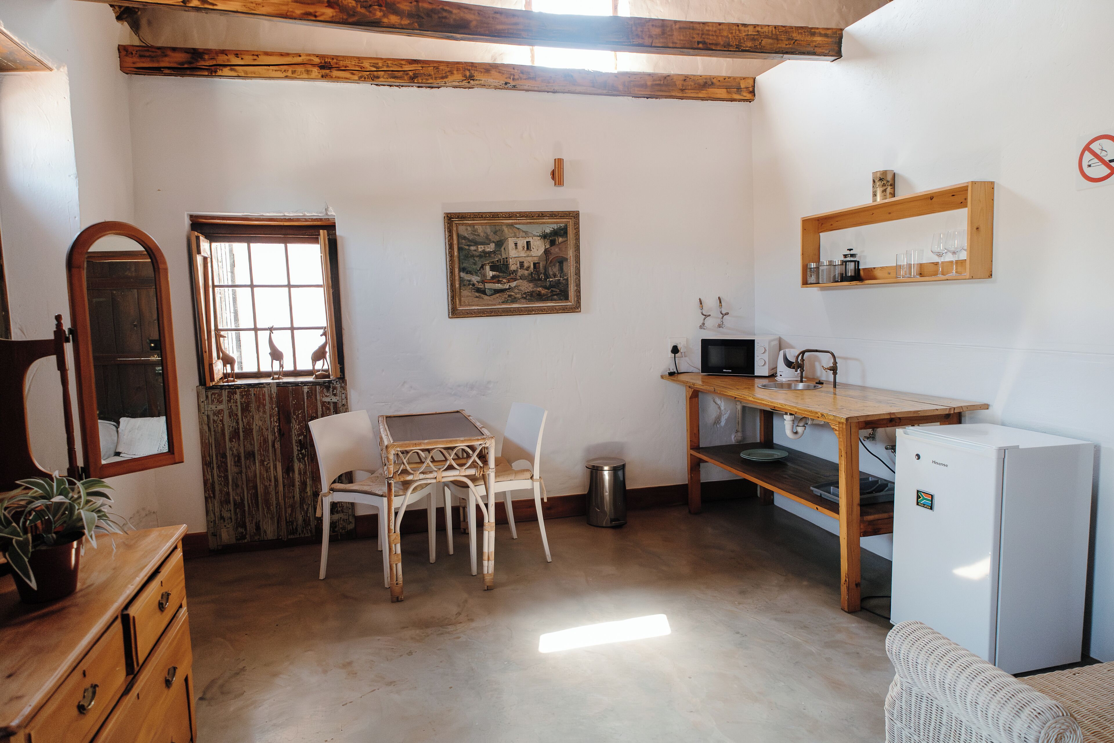 Une cuisine compacte comprenant une table à manger, des chaises, un réfrigérateur et une étagère en bois où sont rangés des verres.