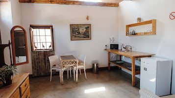 Une cuisine compacte comprenant une table à manger, des chaises, un réfrigérateur et une étagère en bois où sont rangés des verres.