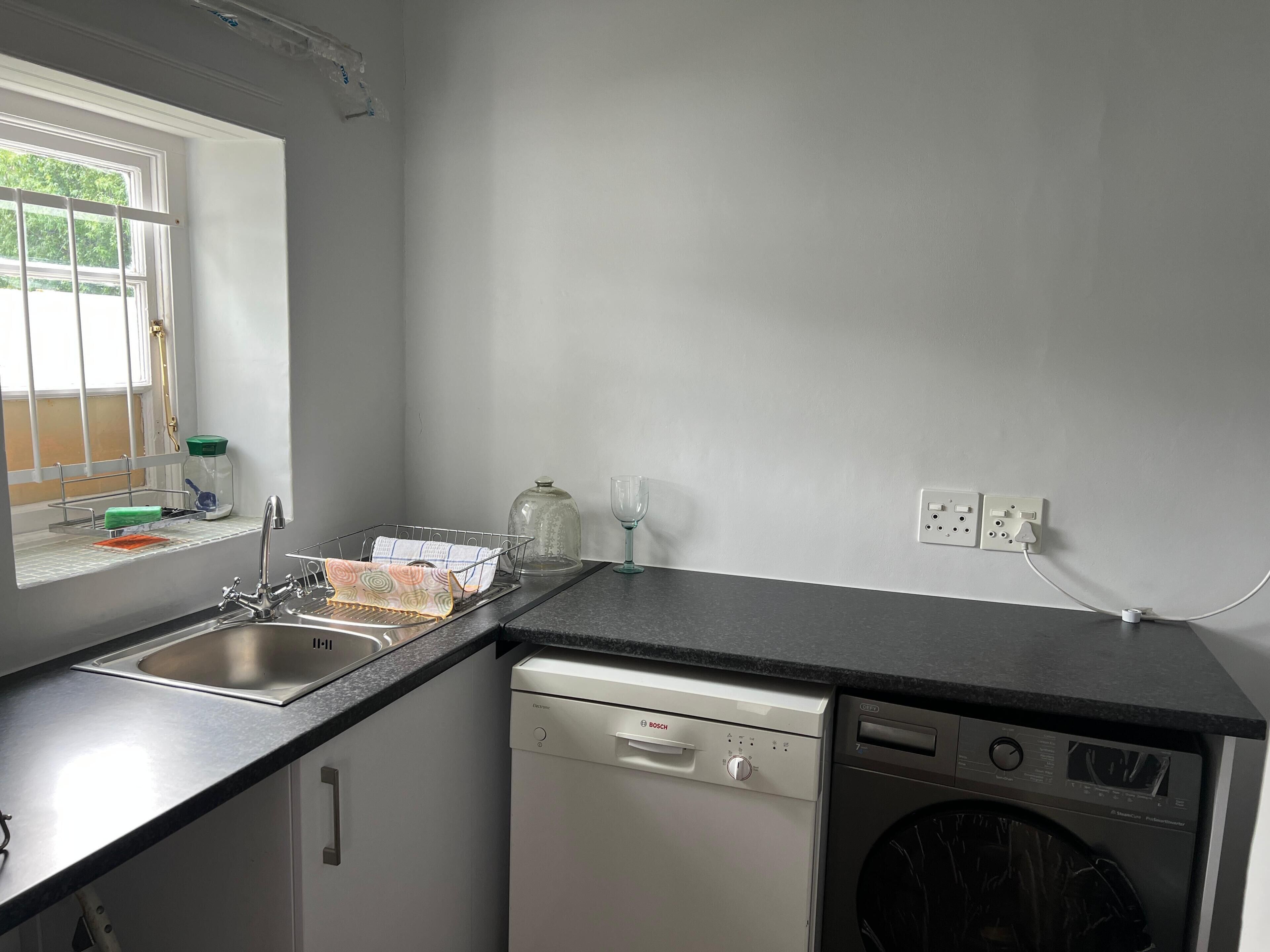 A kitchen with a dishwasher, a washing machine, a window with a view, and a power outlet.