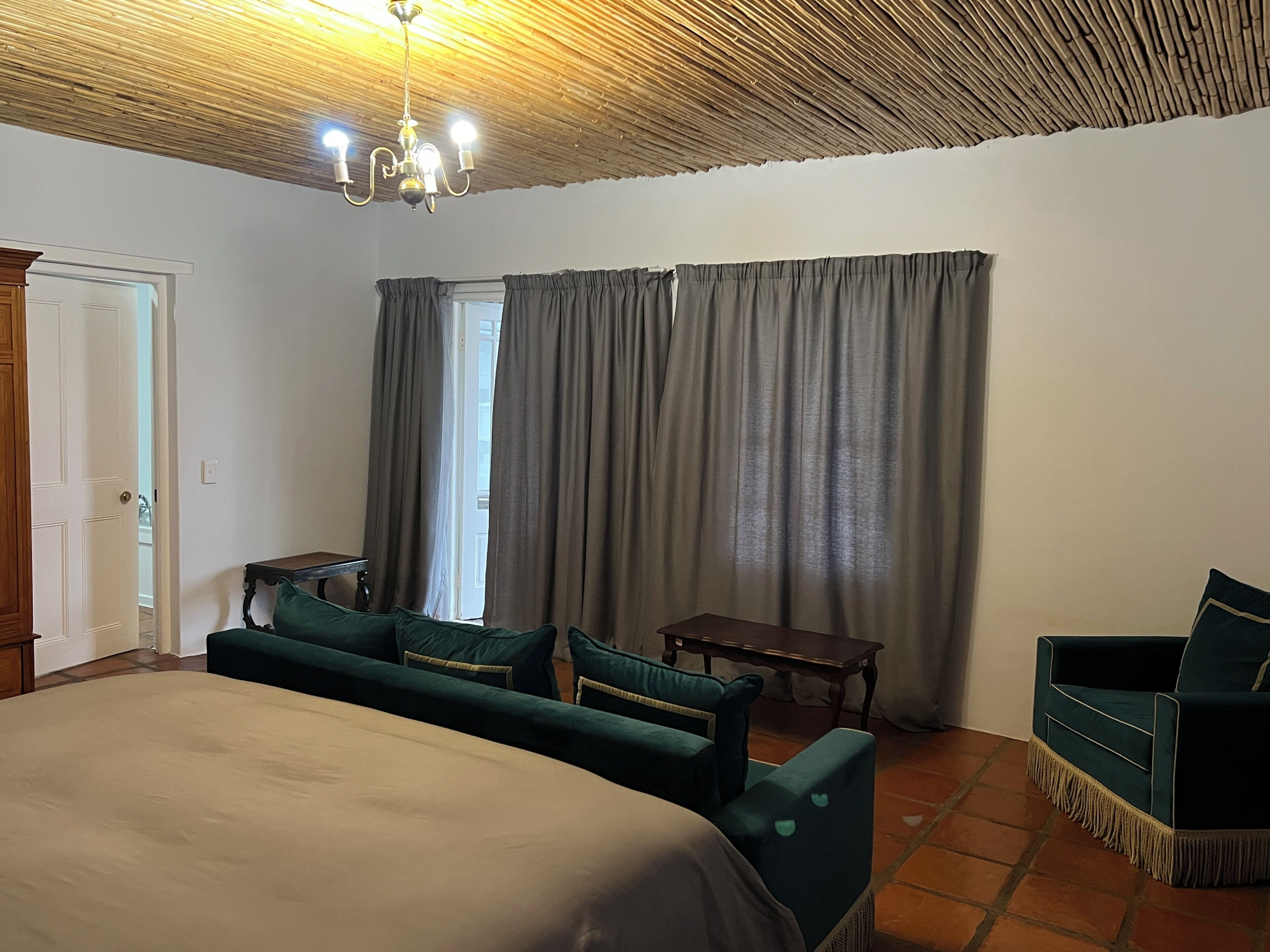 A hotel room with a bed, two armchairs, a small table, a ceiling fan, and a window with curtains.