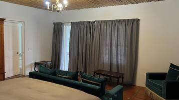 A hotel room with a bed, two armchairs, a small table, a ceiling fan, and a window with curtains.