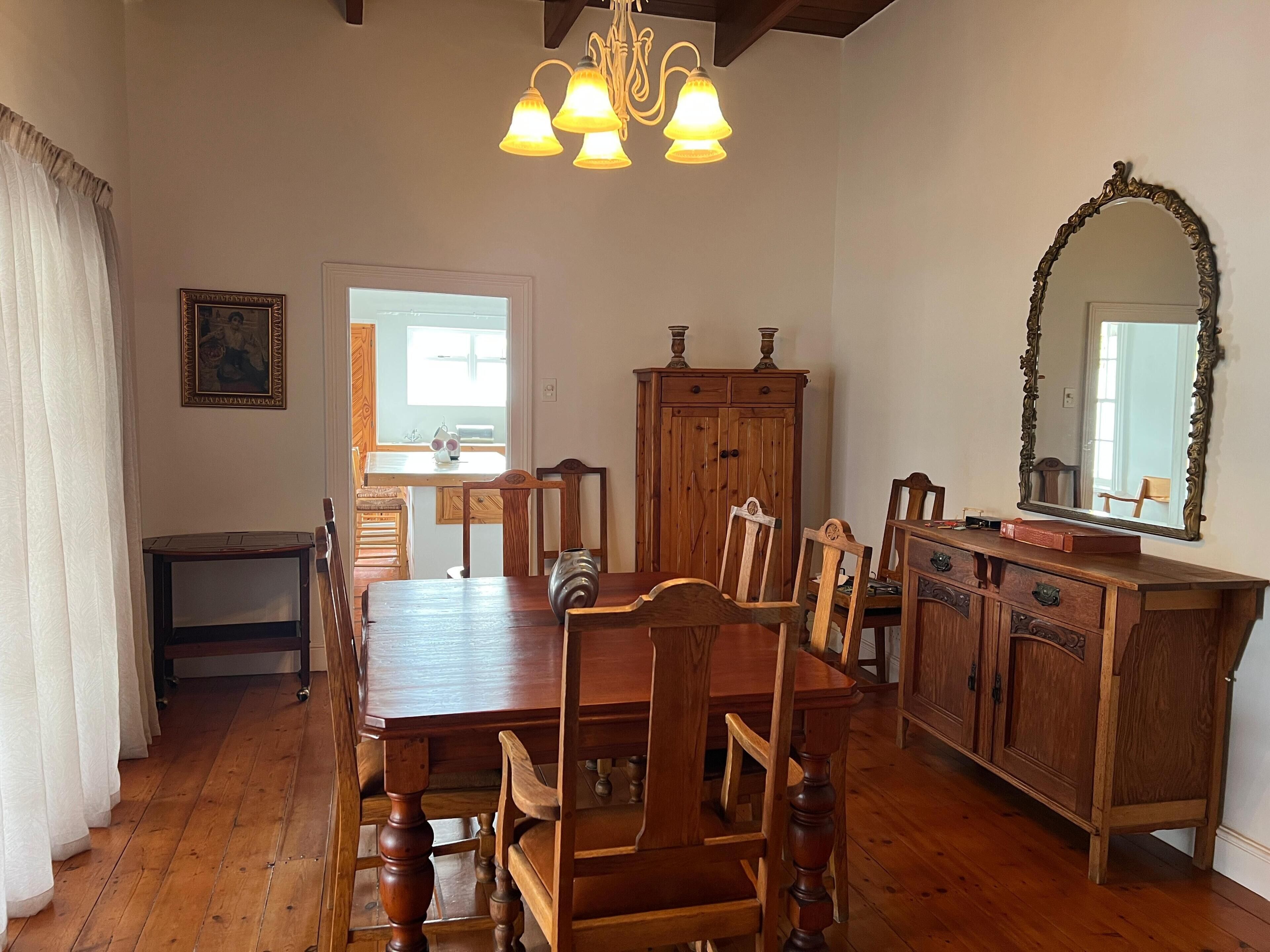 A dining area with a wooden table and chairs, a cabinet, a mirror, and a chandelier.