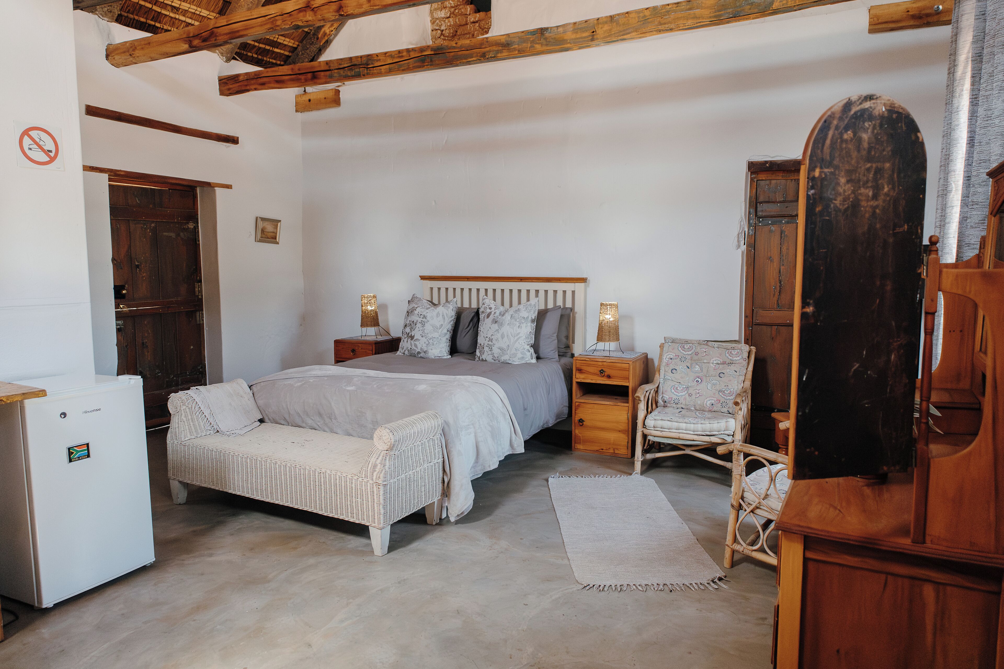 A bedroom with a bed, bedside tables, a chair, a wardrobe, and a small refrigerator.