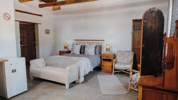 A bedroom with a bed, bedside tables, a chair, a wardrobe, and a small refrigerator.