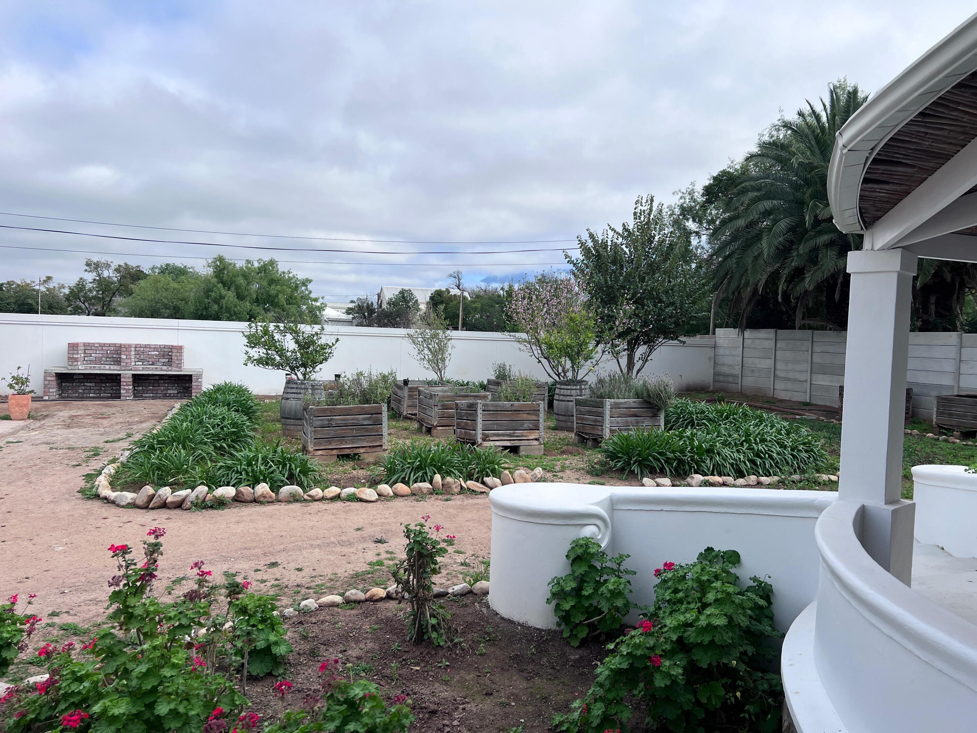Un espace extérieur aménagé avec un barbecue, des jardinières en bois et une structure blanche.