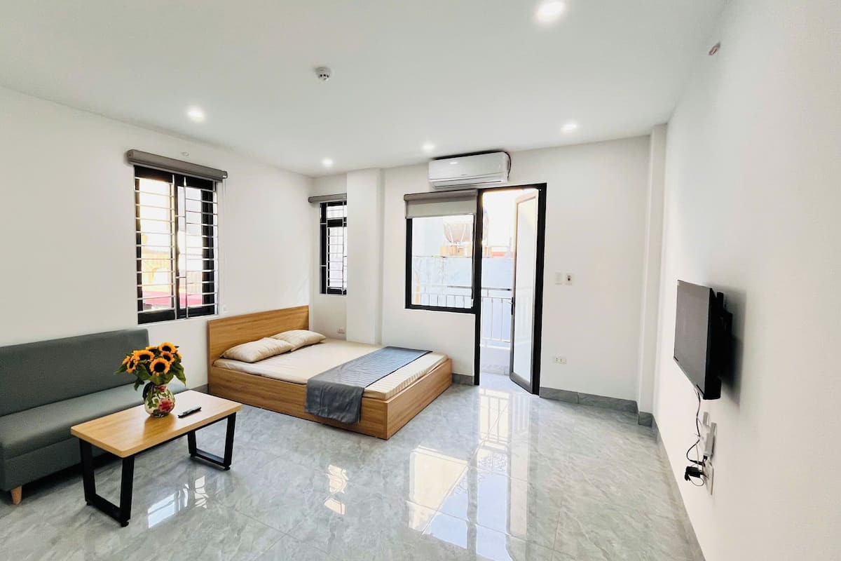 Una habitación de hotel moderna con una cama, un sofá, una mesita con un jarrón de flores y un televisor montado en la pared.