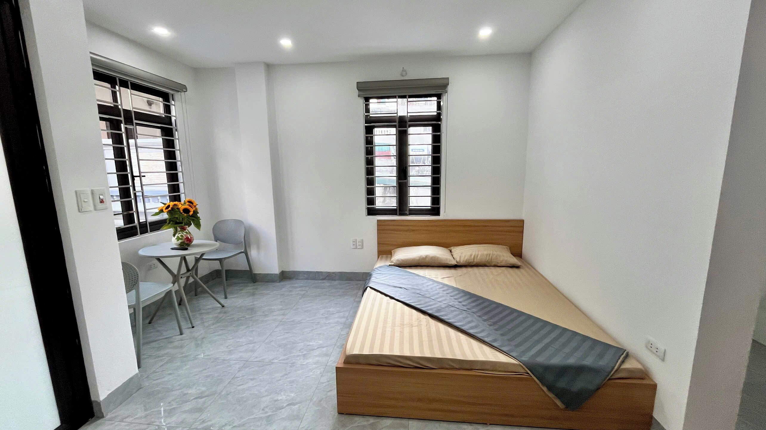 Une petite pièce propre, avec un lit, une chaise, une table et deux fenêtres.