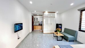 Una sala de estar moderna con un televisor de pantalla plana, un sofá, una mesa de centro y una kitchenette al fondo.