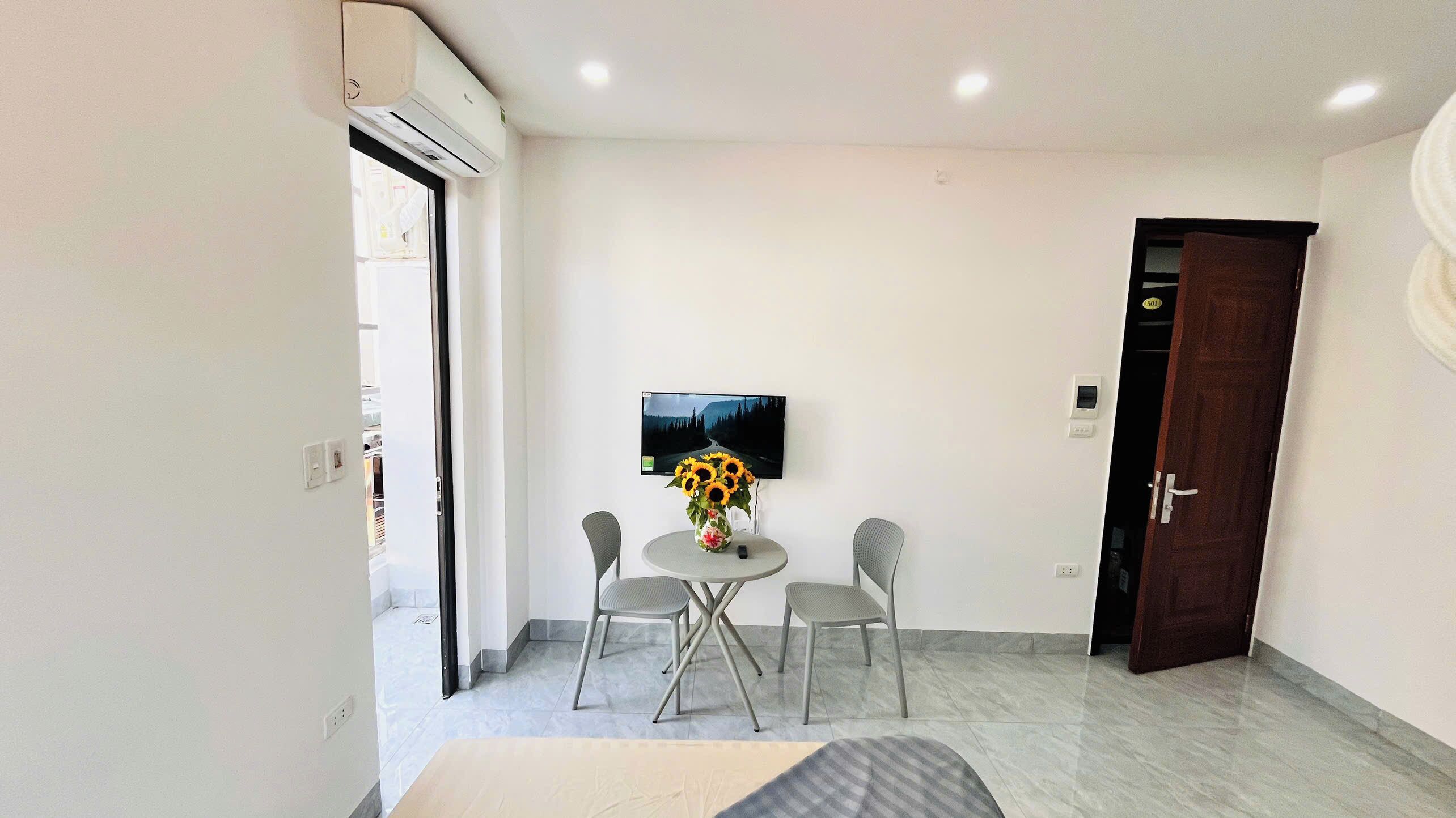 Una habitación pequeña y moderna con una mesa redonda, dos sillas, un televisor en la pared y una puerta.