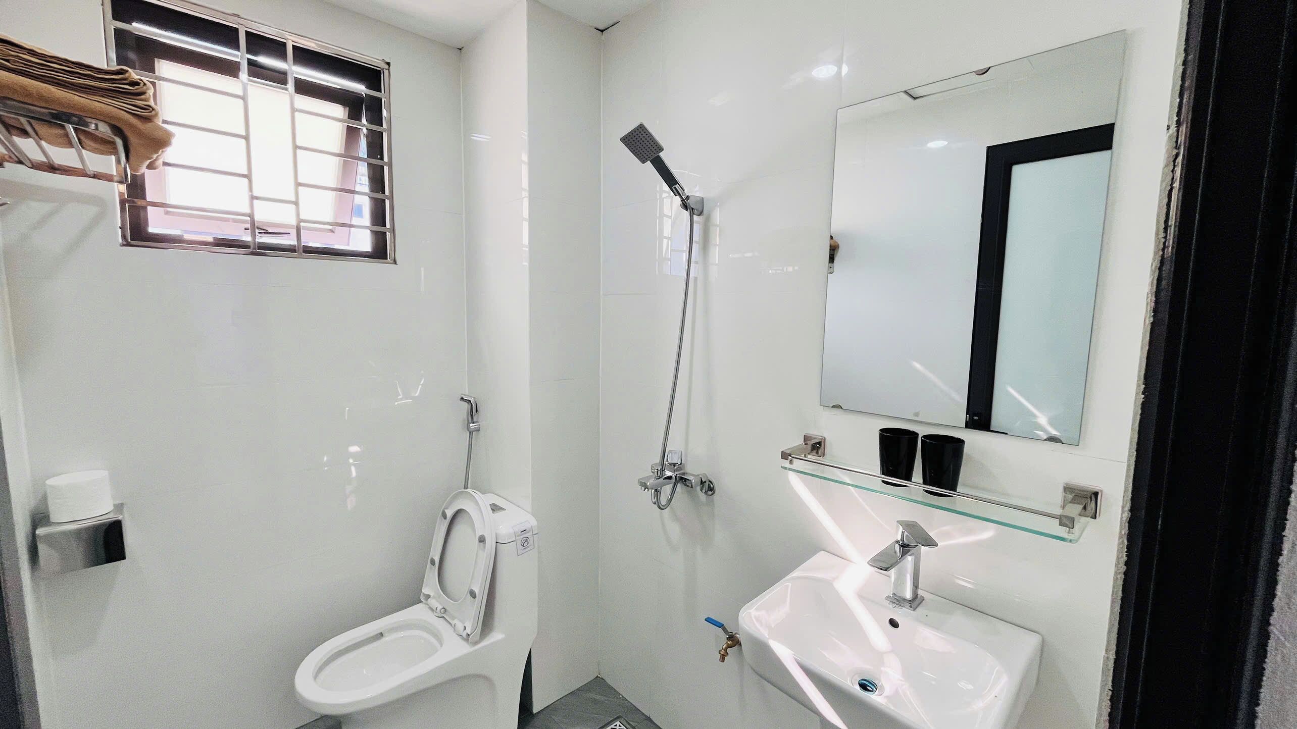 Egy kis, modern fürőszoba, amelyben WC, üvegmosdókagyló, zuhanyzó és tükör található.