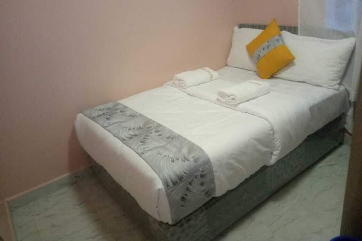 A neatly made bed with white linens, a grey patterned throw, and a yellow pillow.