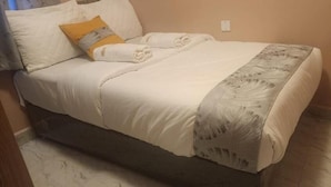 A bed with a white bedspread and a decorative gray accent. - Premier Suites Isiolo (Isiolo)