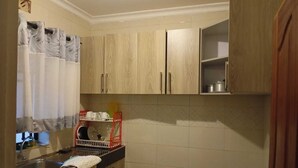 A kitchen with wooden cabinets, a black countertop, and a red dish rack. - Premier Suites Isiolo (Isiolo)
