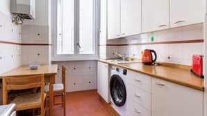 Une cuisine compacte équipée d’un lave-linge, d’un évier et d’une bouilloire rouge.