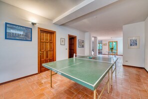 A spacious room with a ping pong table, wooden doors, and framed pictures on the walls.