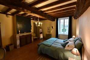 Un dormitorio con una cama grande, vigas de madera, una chimenea de piedra y una ventana con cortinas.