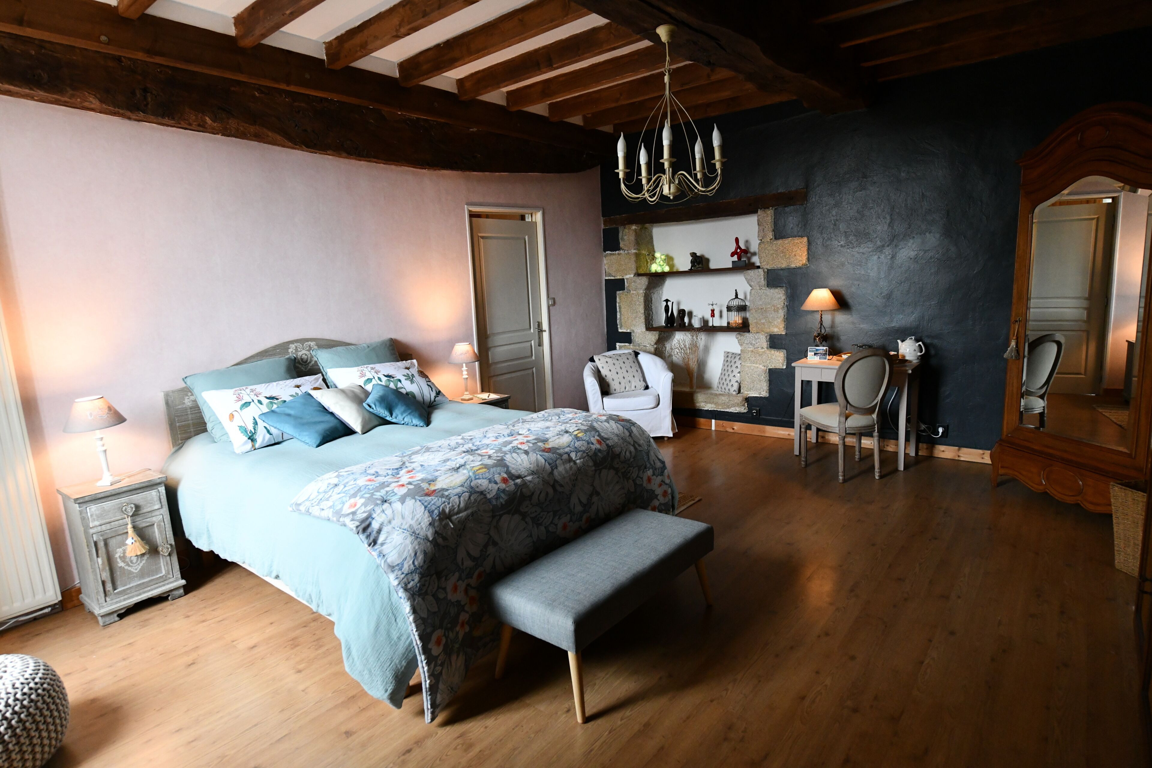A bedroom with a bed, bench, nightstands, a chair, a small table, and a mirror.