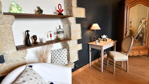 Ett rum med en säng, ett skrivbord, en stol, en spegel och en hylla med dekorativa föremål.