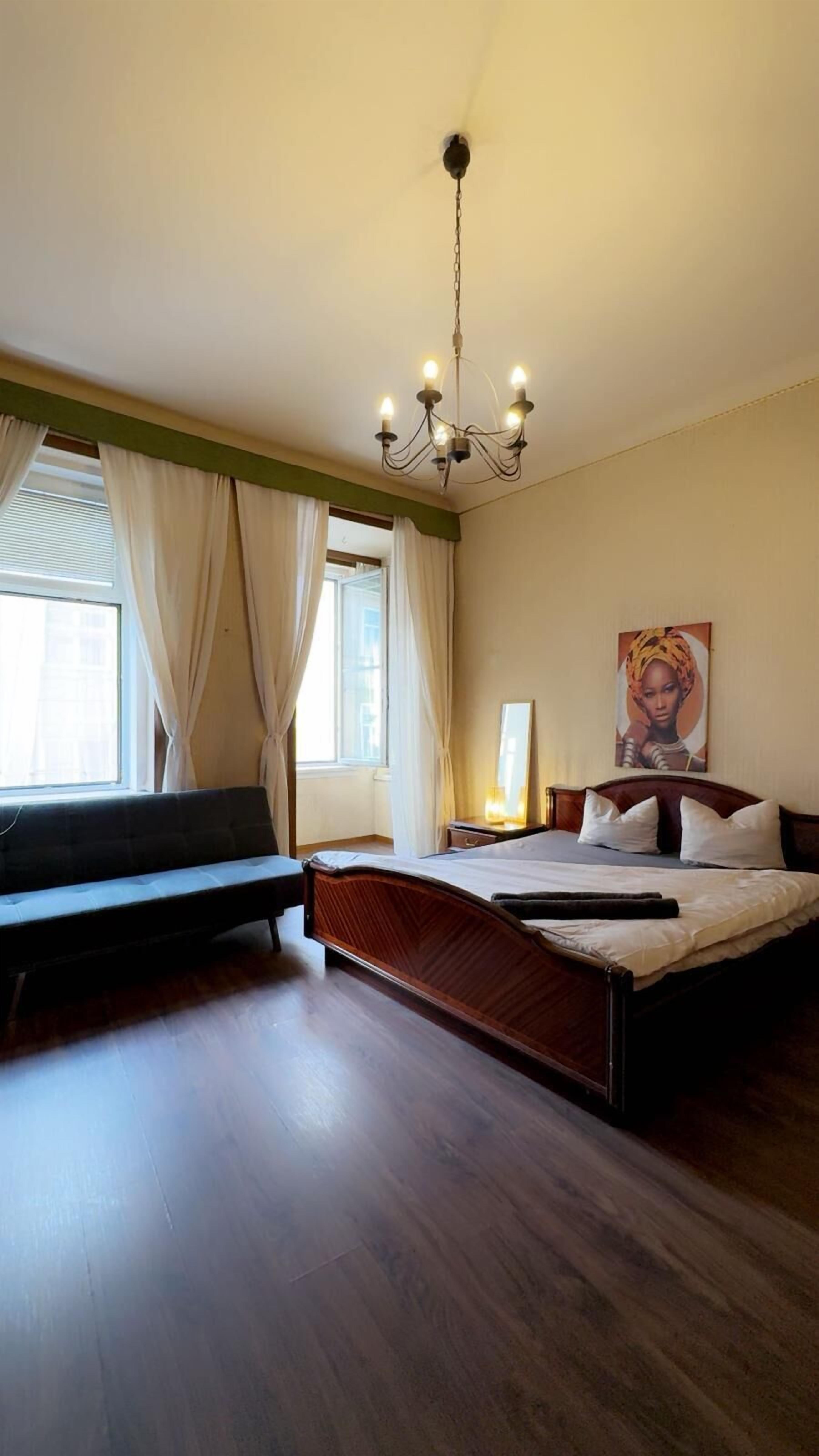 Una camera da letto con un letto grande, un comodino, una lampada a sospensione e una finestra con tende.