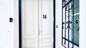 Une porte blanche à deux battants, portant le numéro 14, une petite fenêtre ornée de barreaux en fer décoratifs et un carillon situé à gauche.