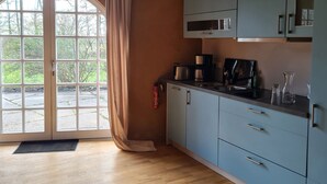 Une cuisine équipée d’un four à micro-ondes, d’un grille-pain et d’une machine à café sur le plan de travail, d’un extincteur et offrant une vue sur l’extérieur grâce à une grande fenêtre munie d’un rideau.