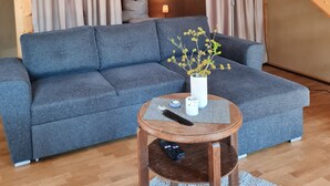 Une pièce de style loft avec un escalier en bois, un canapé gris, une petite table ronde et une lampe.