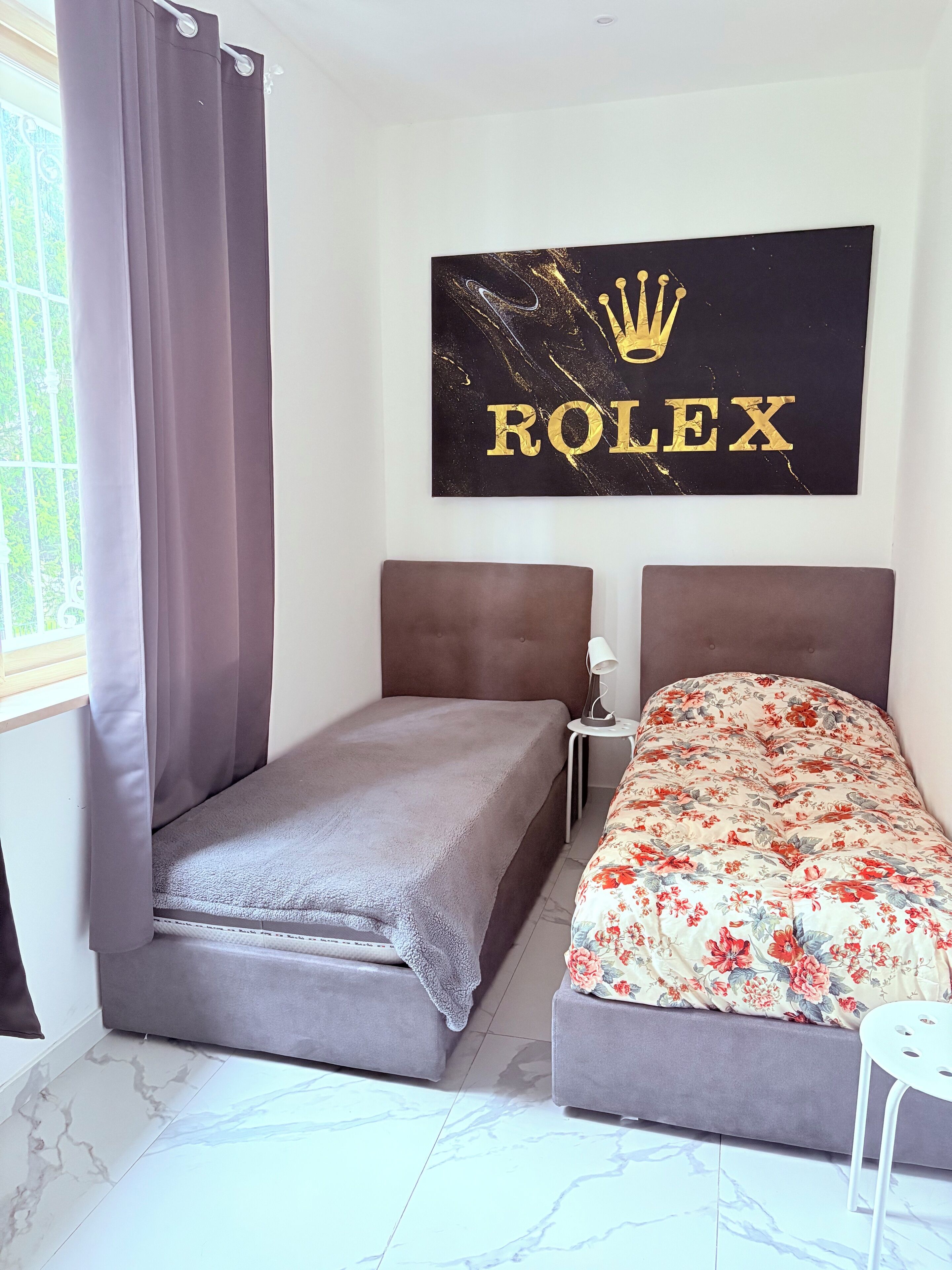 Ein Schlafzimmer mit einem Bett, einem Nachttisch, einem Wandbild und einem Fenster mit Vorhängen.