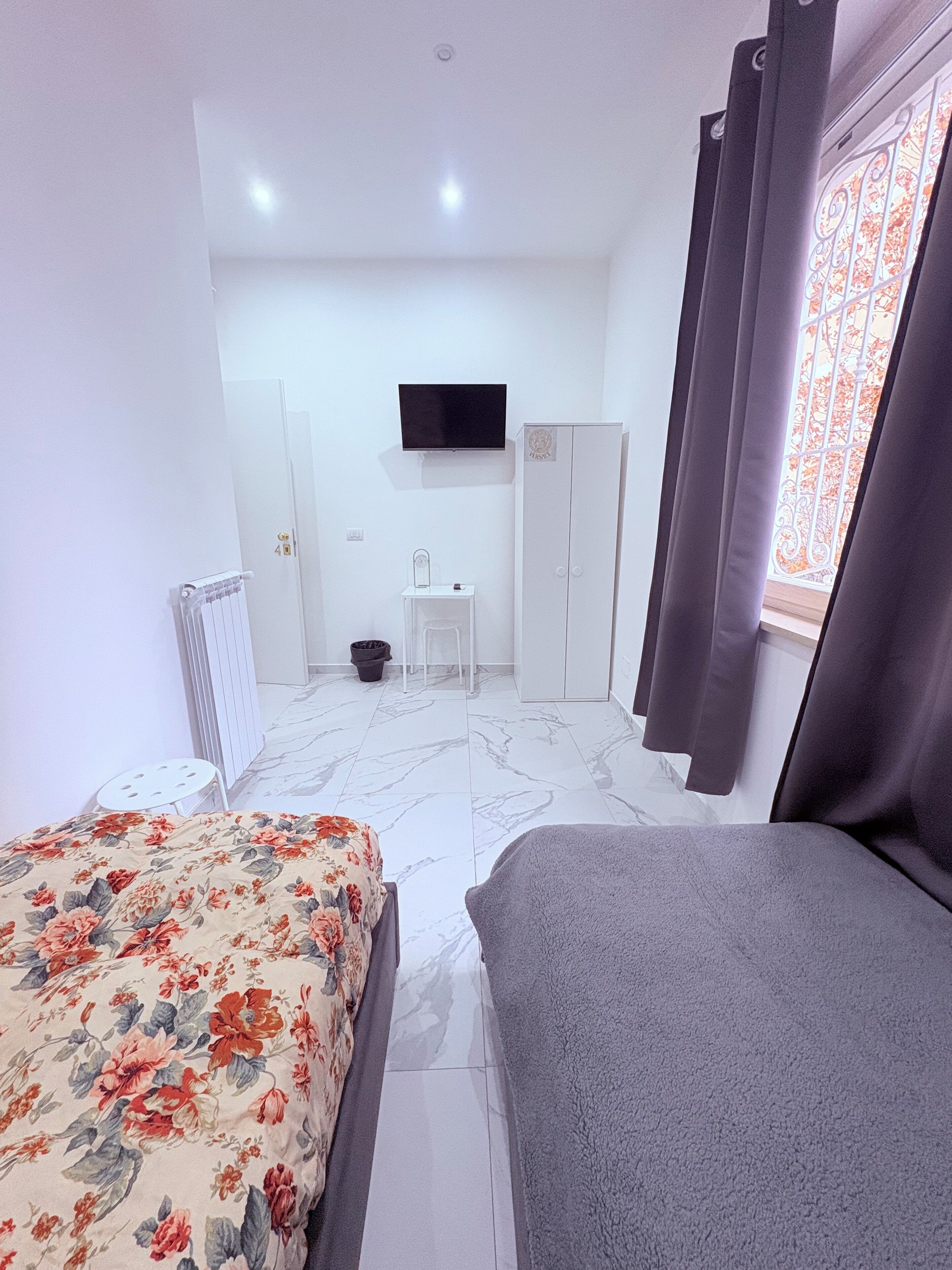 A bedroom with a bed, a TV, a wardrobe, and a window with curtains.