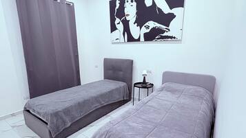 Ein modernes Schlafzimmer mit zwei Betten, einem grauen Vorhang, einem kleinen Tisch mit einer Lampe und einem großen Schwarz-Weiß-Kunstwerk an der Wand.