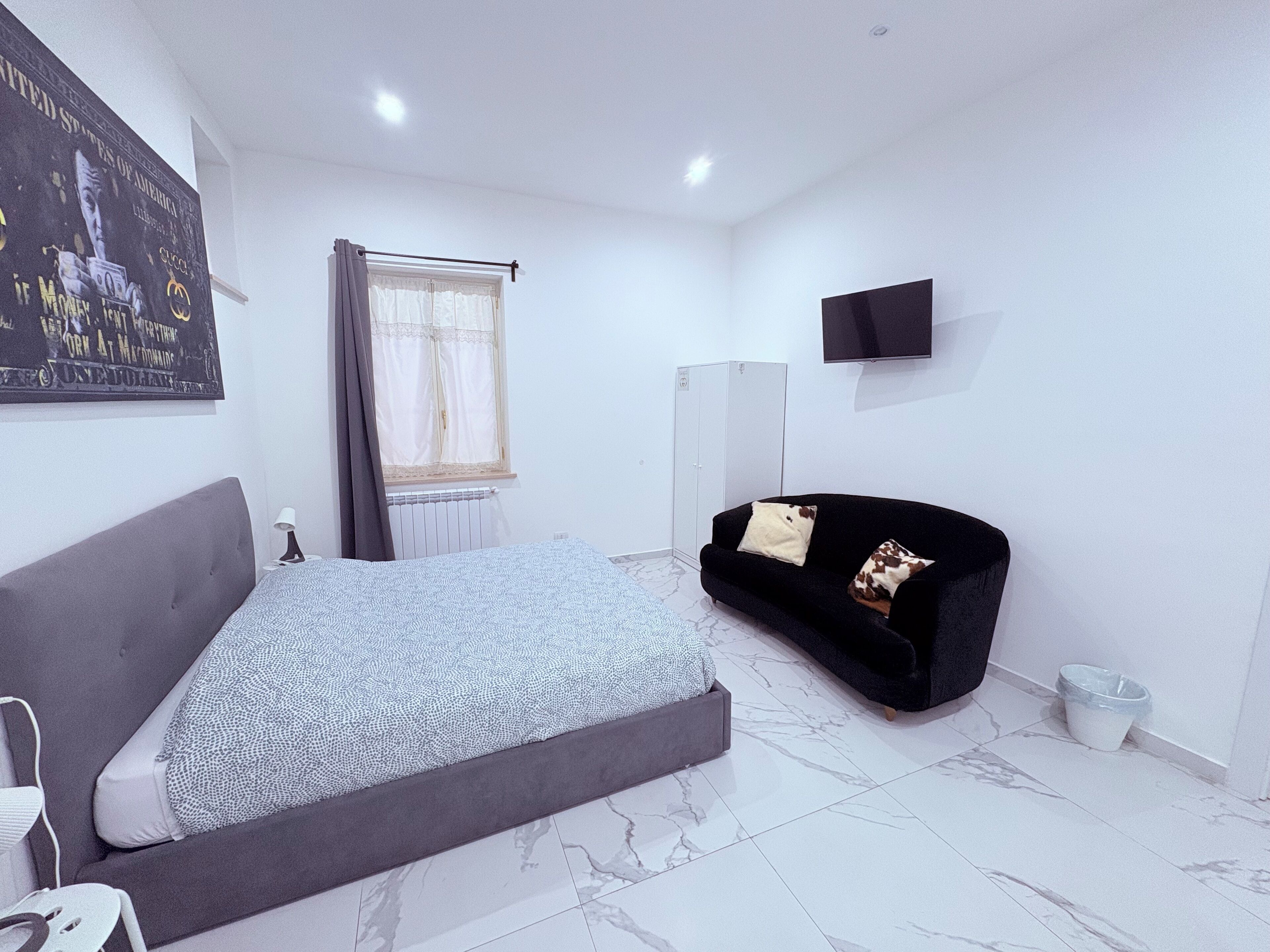 A bedroom with a bed, a black sofa, a TV, and a poster on the wall.