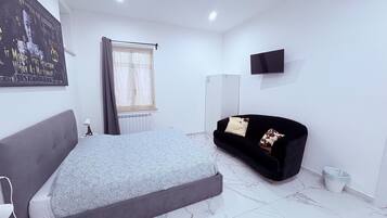 A bedroom with a bed, a black sofa, a TV, and a poster on the wall.