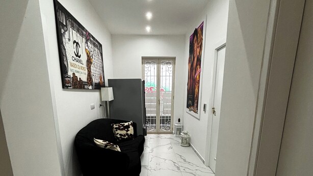 A narrow hallway with a black sofa, marble flooring, and two large posters on the walls. - Villa Life  (San Donato Milanese)