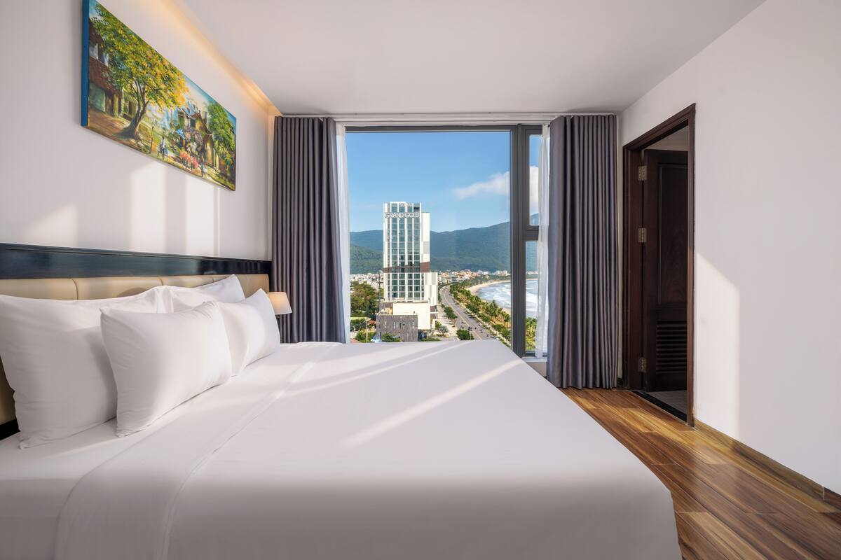 Une chambre d’hôtel avec un grand lit, un tableau au mur et une vue sur le paysage urbain par la fenêtre.
