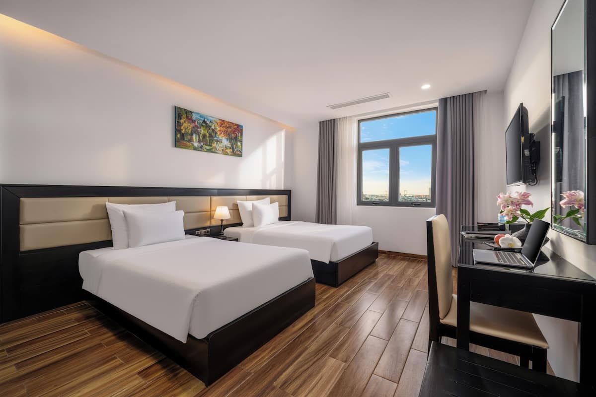 Une chambre d’hôtel avec deux lits, un bureau avec un ordinateur portable, une télévision et une grande fenêtre donnant sur la ville.