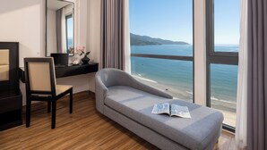 Une chambre d’hôtel moderne dotée d’une grande fenêtre donnant sur la mer et les montagnes lointaines.