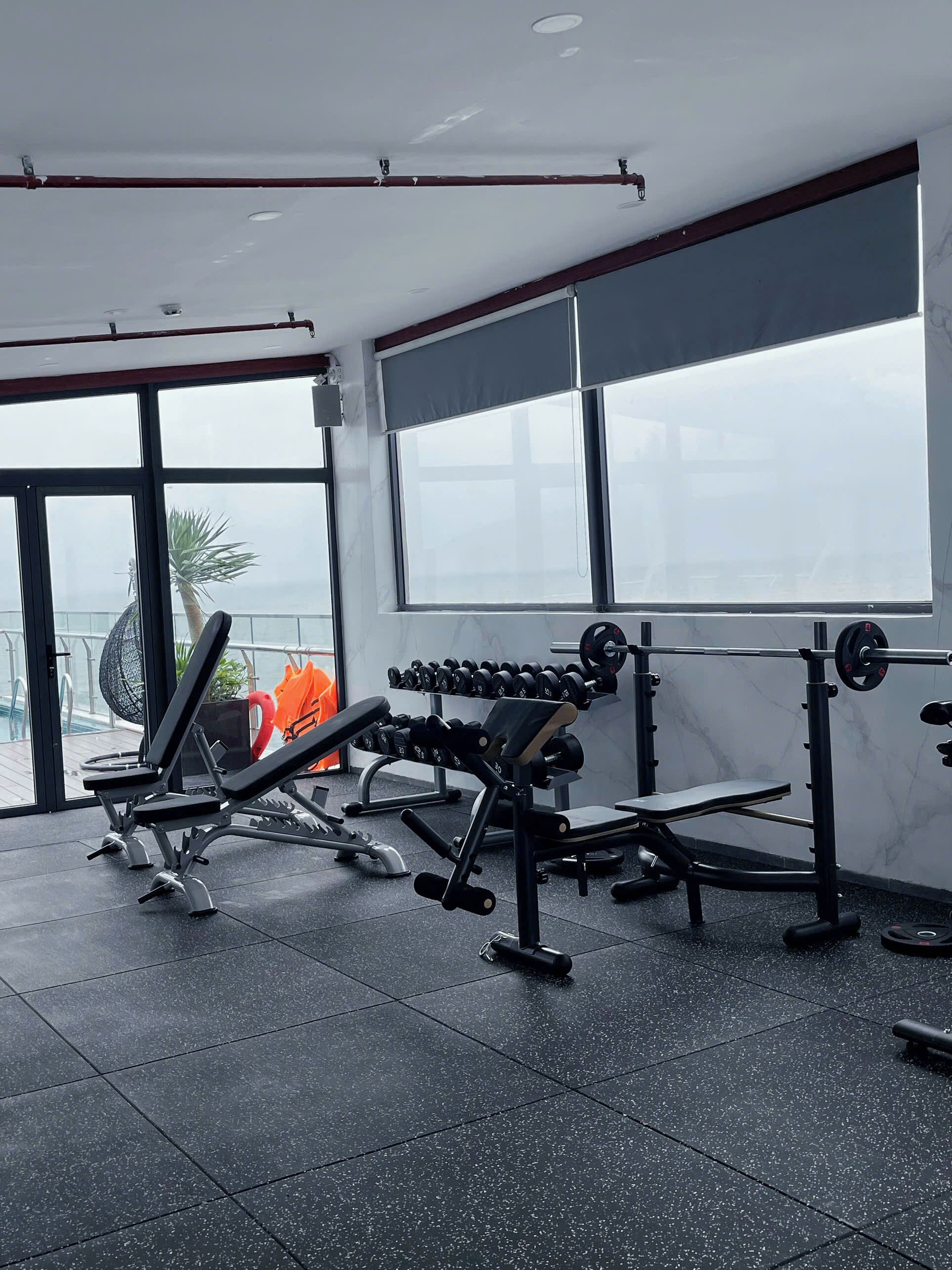 A gym with weightlifting equipment, large windows, and a view of the outside.