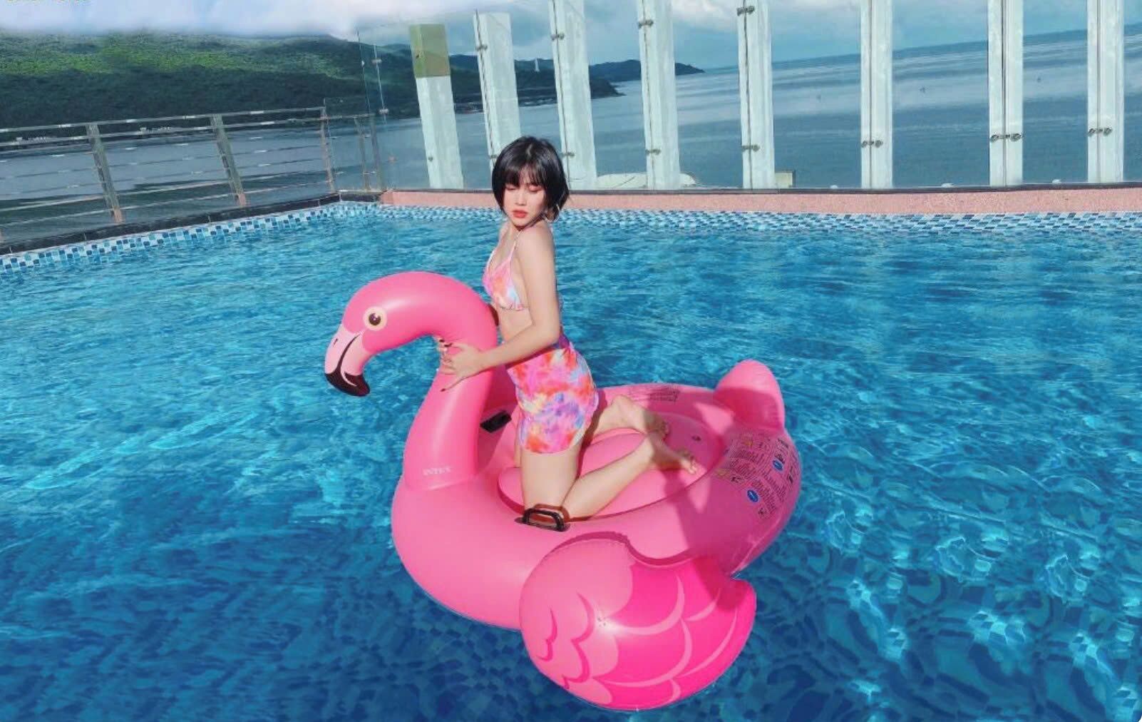 A pool with clear blue water, a person on a pink flamingo float, and a view of the sea in the background.