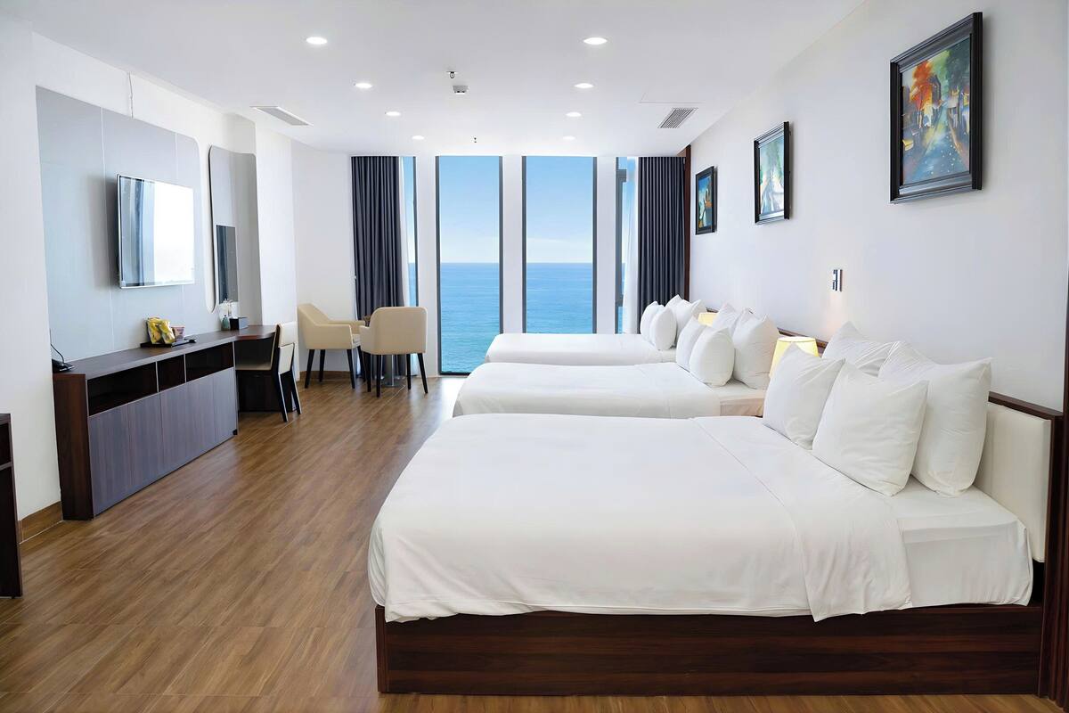 Une chambre d’hôtel avec deux lits, un bureau, une chaise, une télévision et de grandes fenêtres donnant sur la mer.